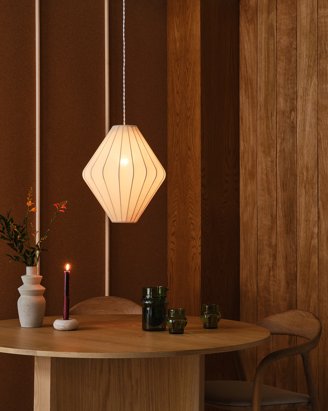 Gemütliche Ecke mit einer weißen Papier-Pendelleuchte über einem runden Holztisch, dekoriert mit Vasen und Kerzen